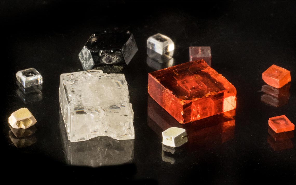 Photo of six blocky-shaped mineral crystals that are either clear or semi-opaque white or orange.
